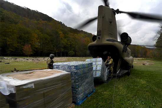 Helicopter with service members unloading water bottle pallets, etc.