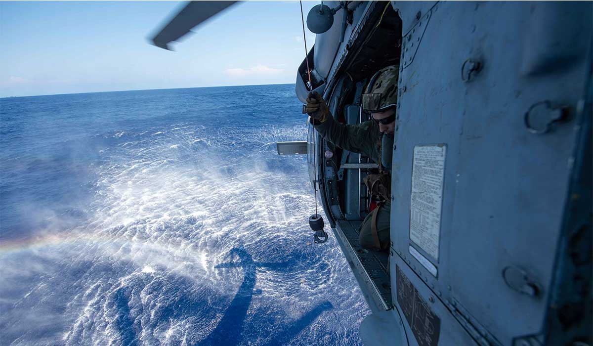 Service member looks down to the ocean from a helicopter.