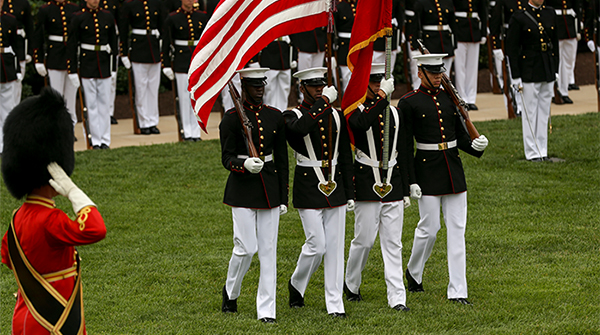 Service members at Marine Corps ceremony carrying flags.