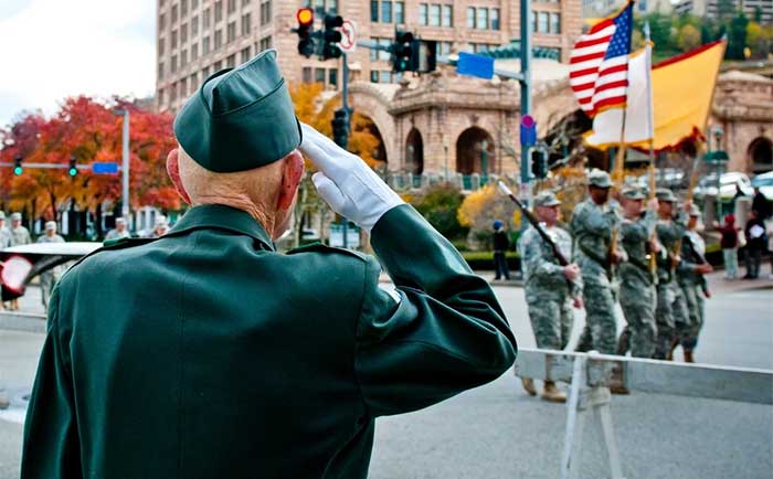 Service member saluting group of service members holding flags marching in a parade