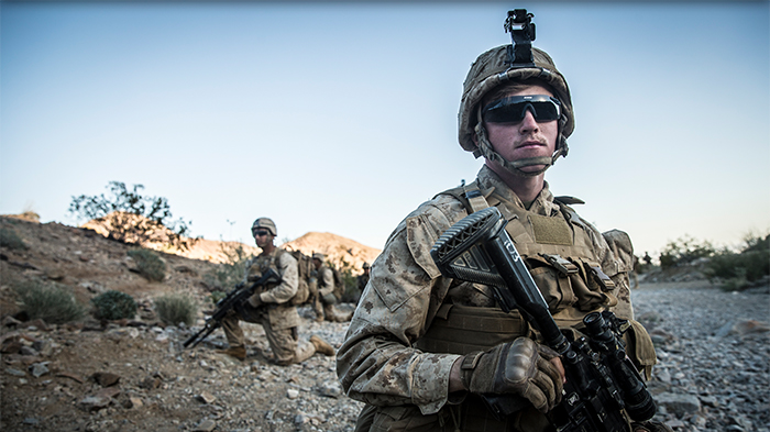 Two service members look into camera while holding guns. 