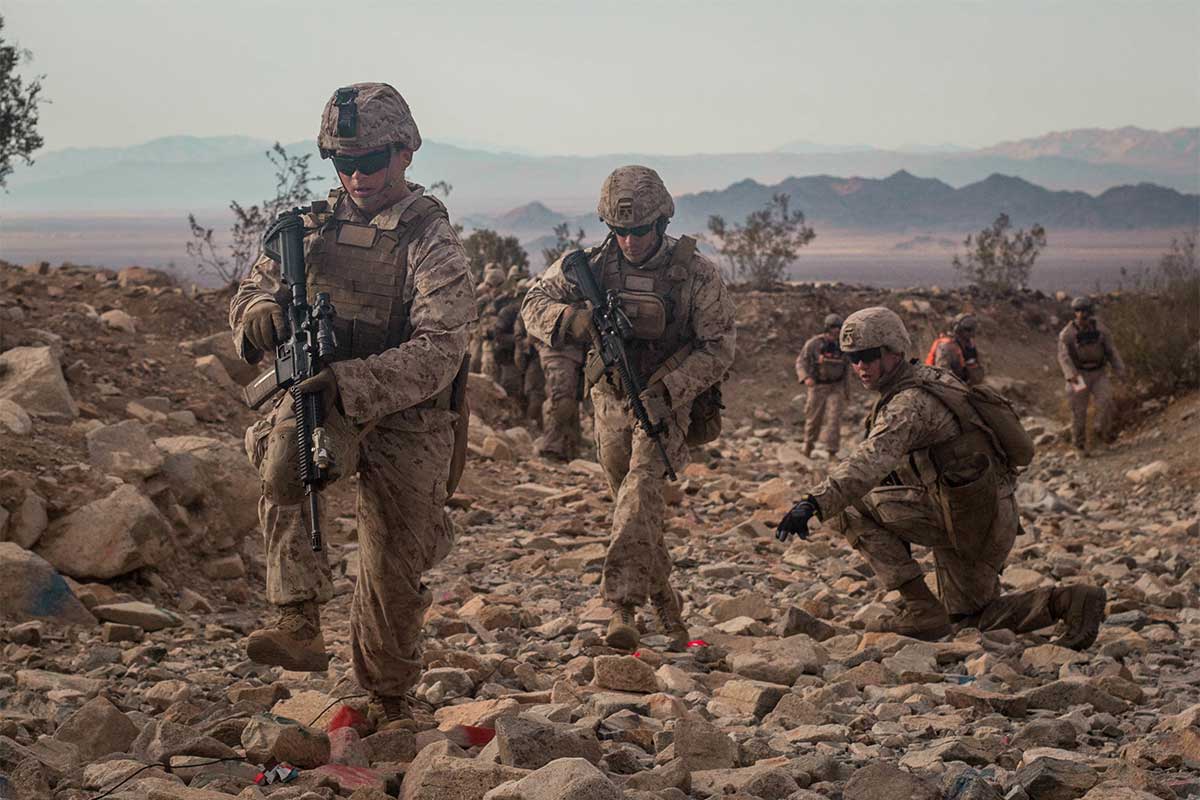 Group of service members walk through rocky terrain.