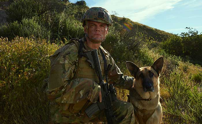 Service member sitting on a hill beside a dog