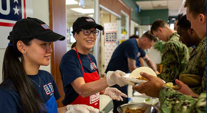 USO volunteer hands service member a meal